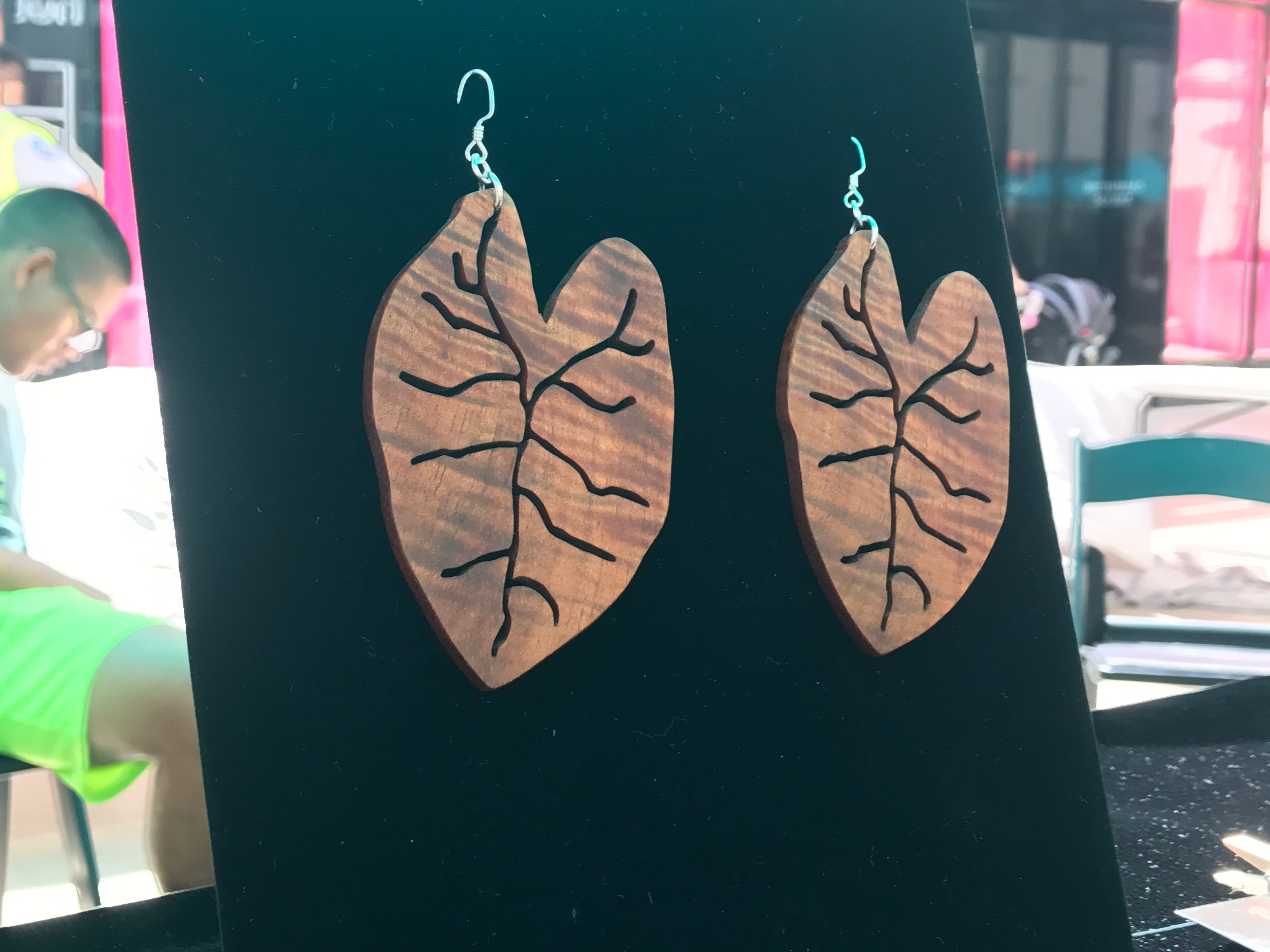 Wooden leaf-shaped earrings with vein detailing on dark teal background