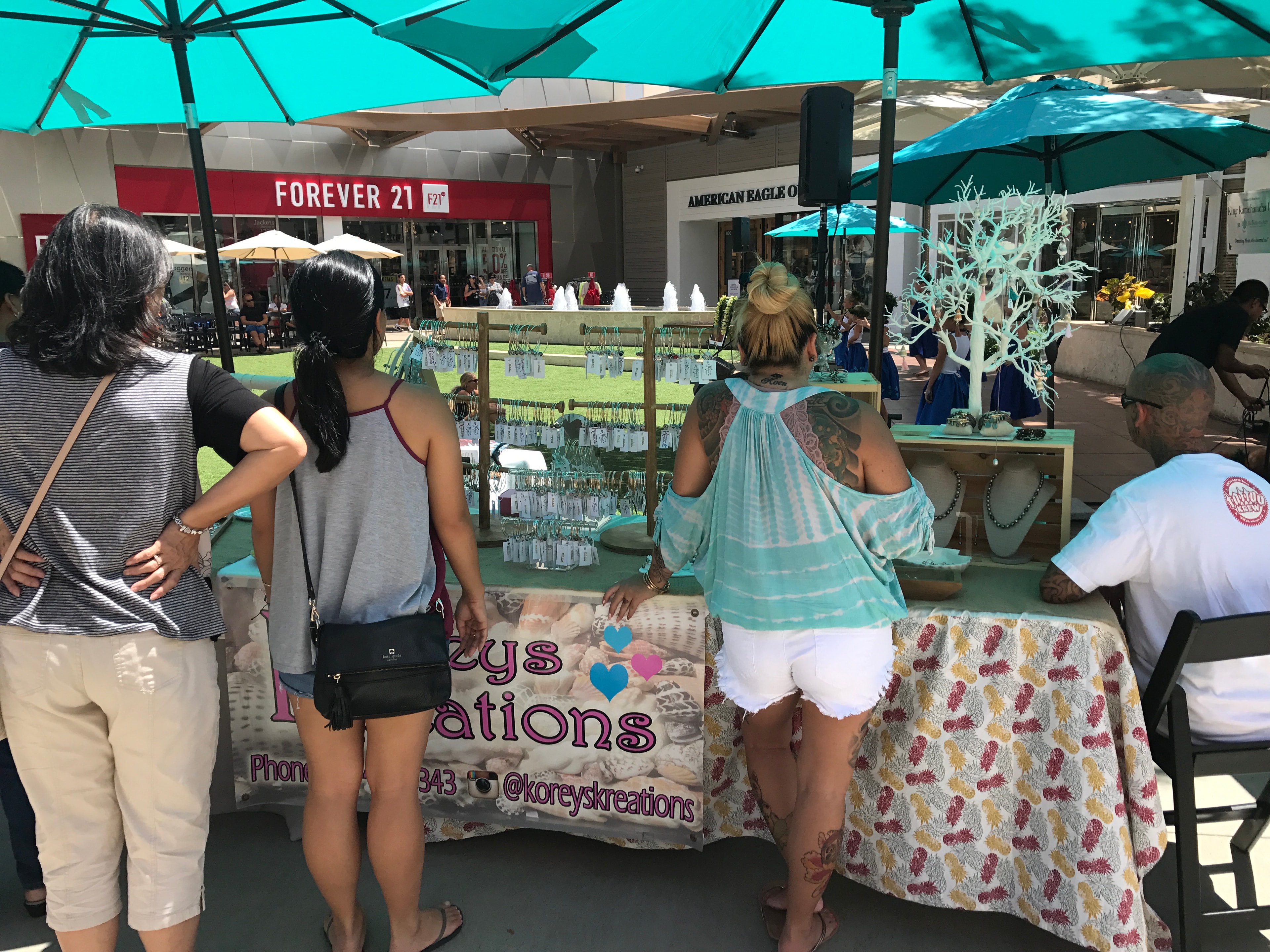 Outdoor market vendor booth with shoppers under teal umbrellas