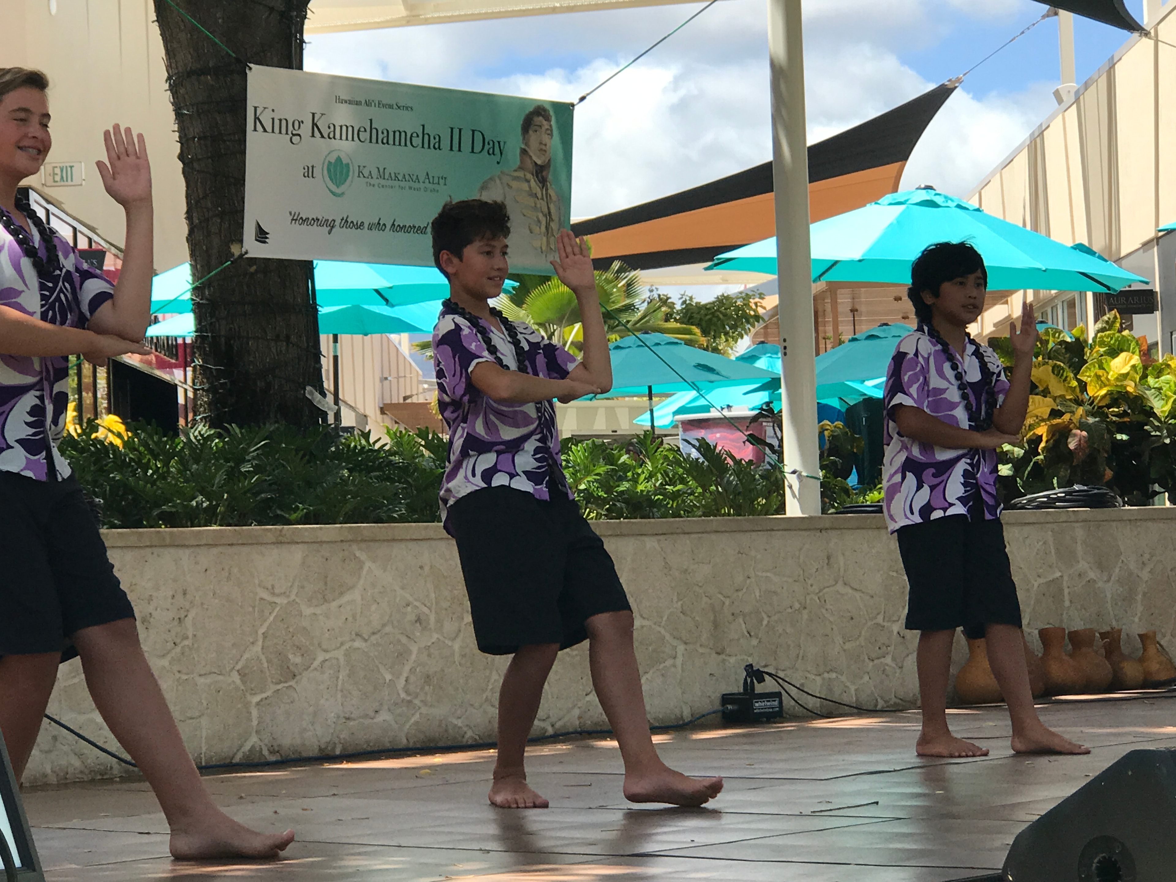 Young male hula dancers in purple and white performing at King Kamehameha II Day outdoor stage