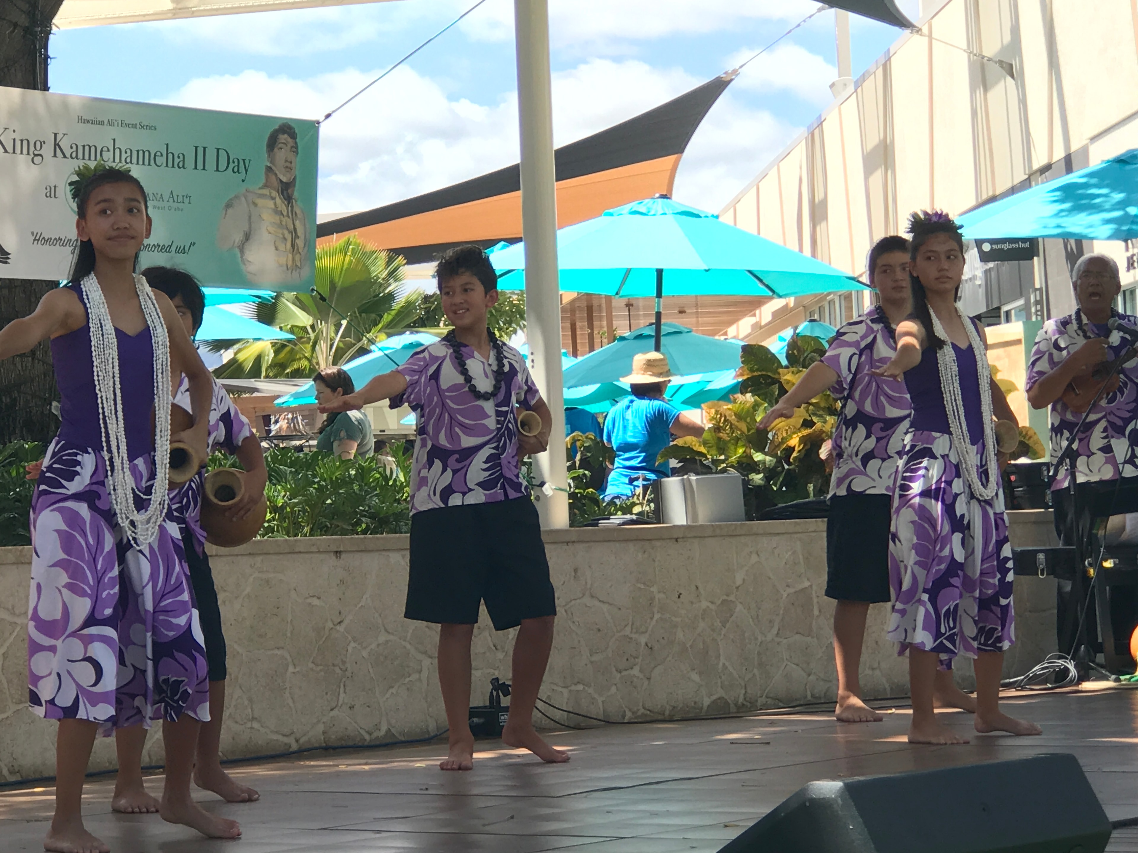 Hula dancers and musicians in purple attire performing with ipu gourds at King Kamehameha II Day