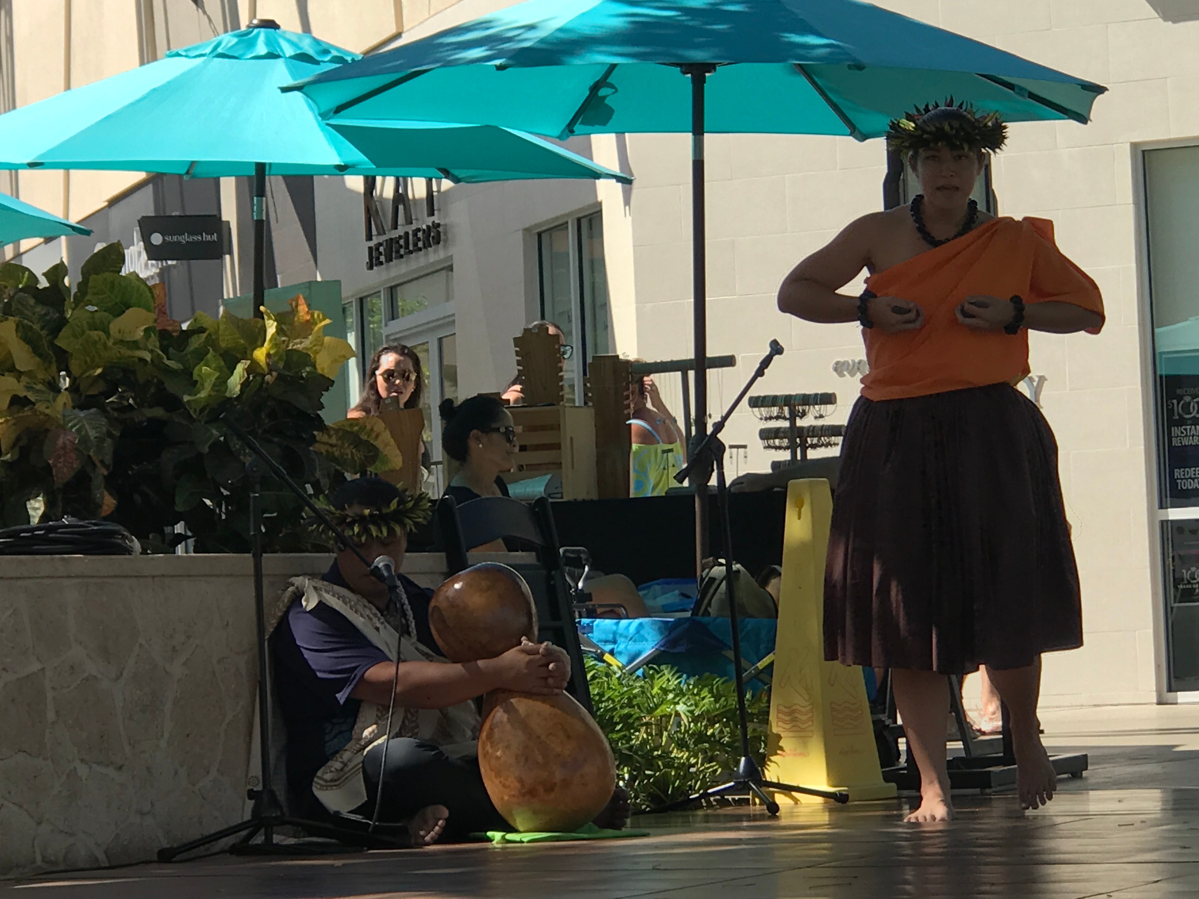 Hula dancer in orange kapa with ipu gourd drummer performing at outdoor King Kamehameha II Day stage