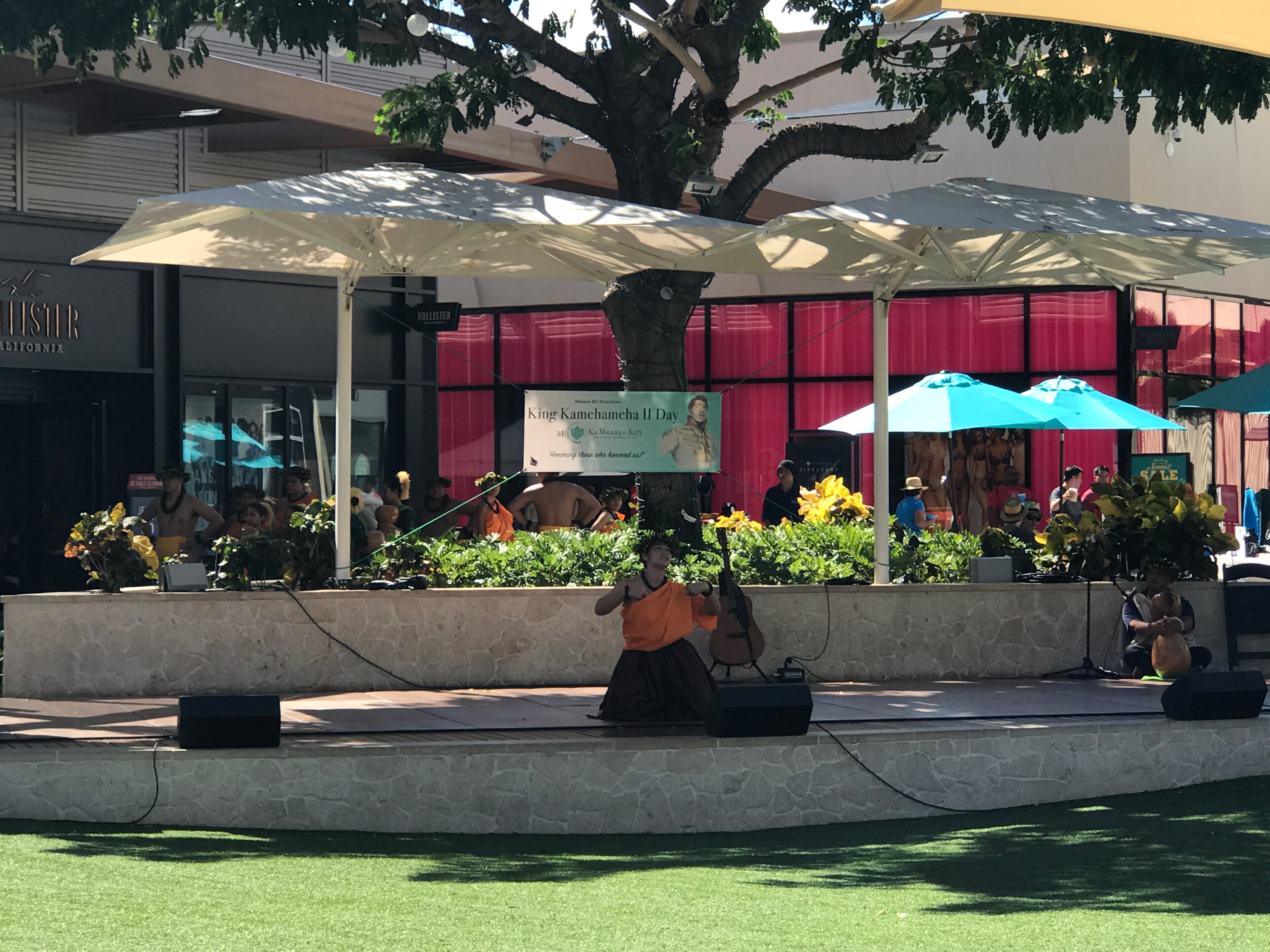 Wide view of King Kamehameha II Day stage at Ka Makana Alii with performers and audience on lawn