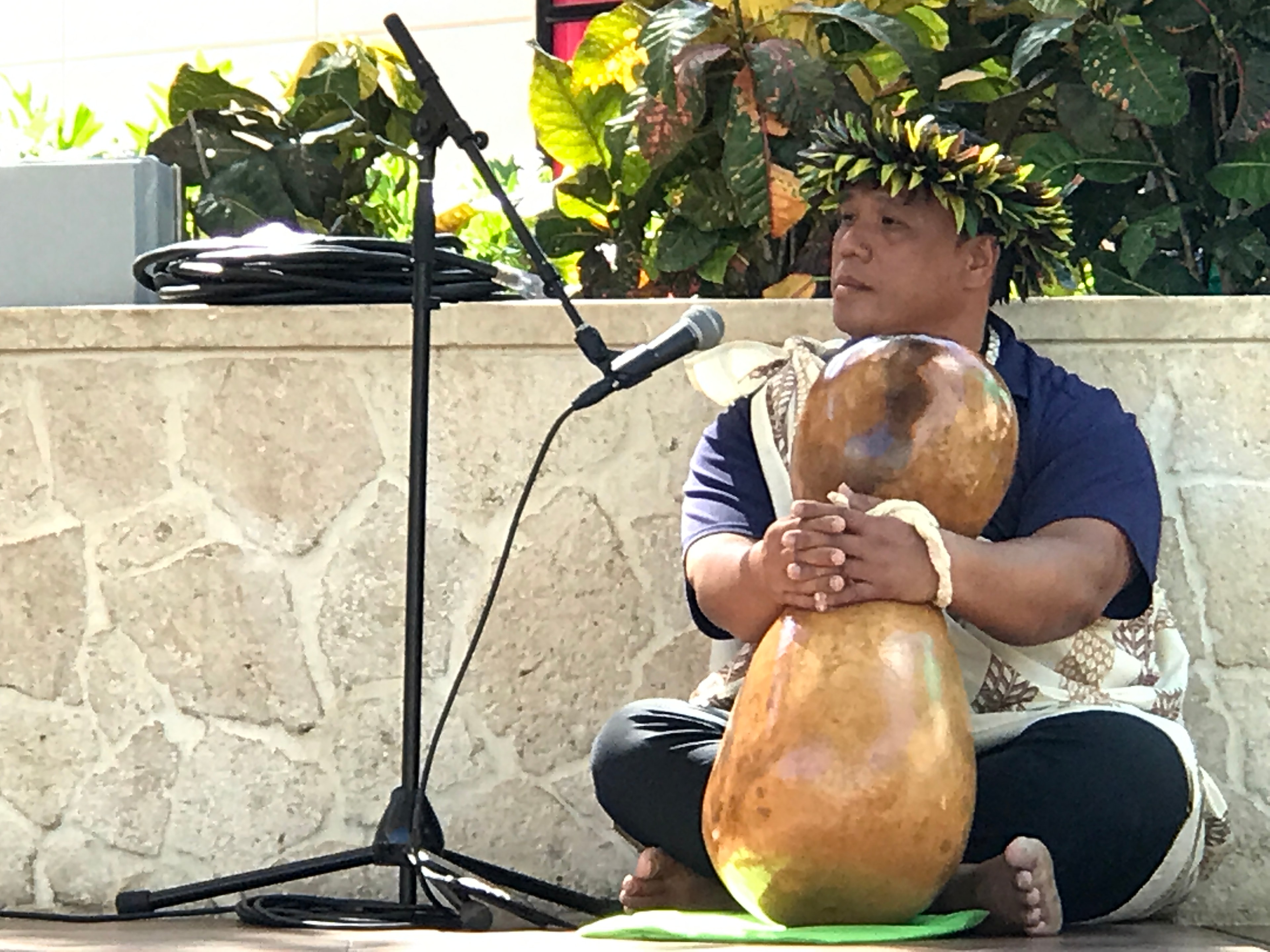 Musician seated with large ipu gourd drum at King Kamehameha II Day outdoor stage