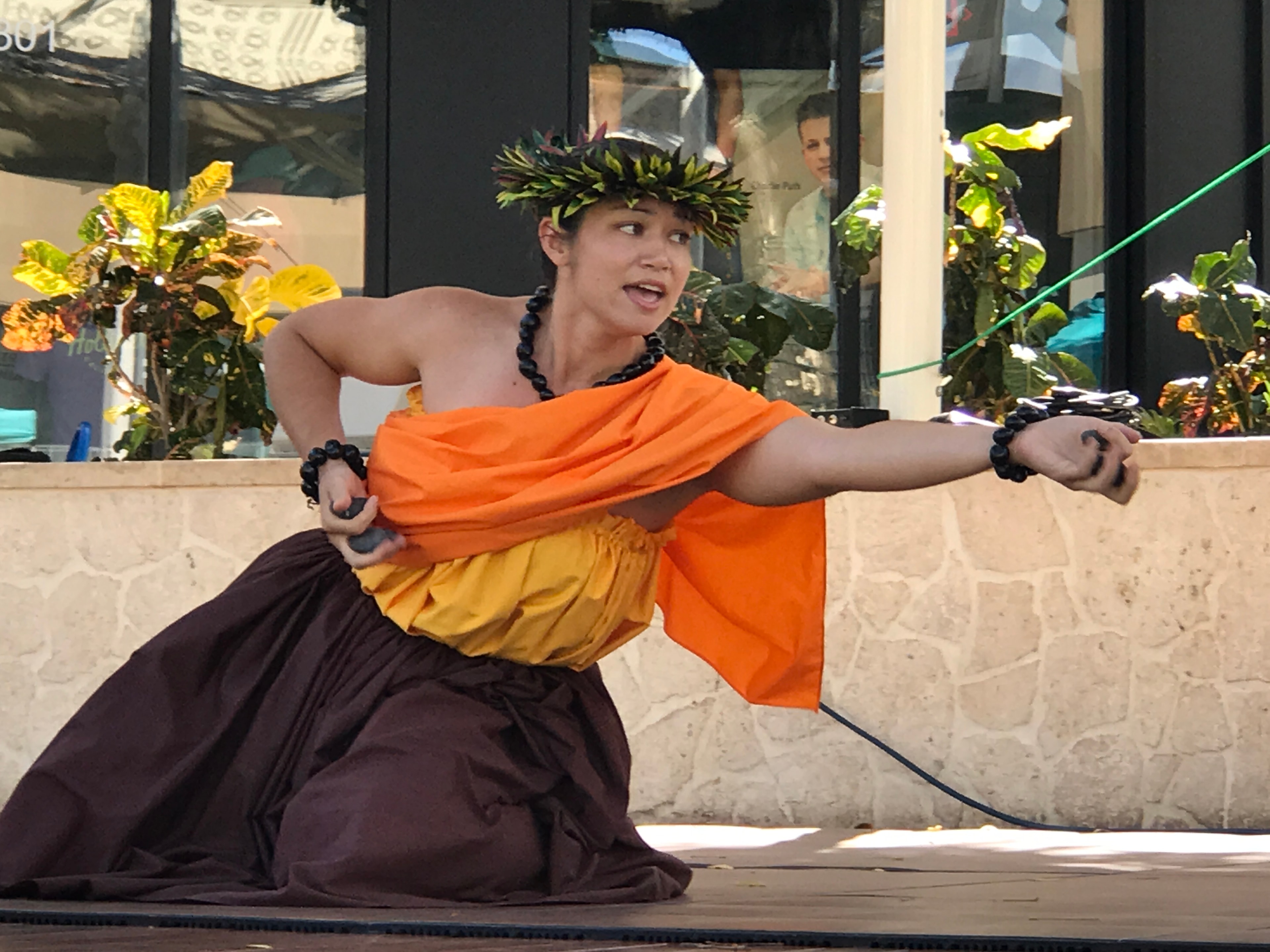 Hula dancer in orange kapa kneeling with arms extended at King Kamehameha II Day stage
