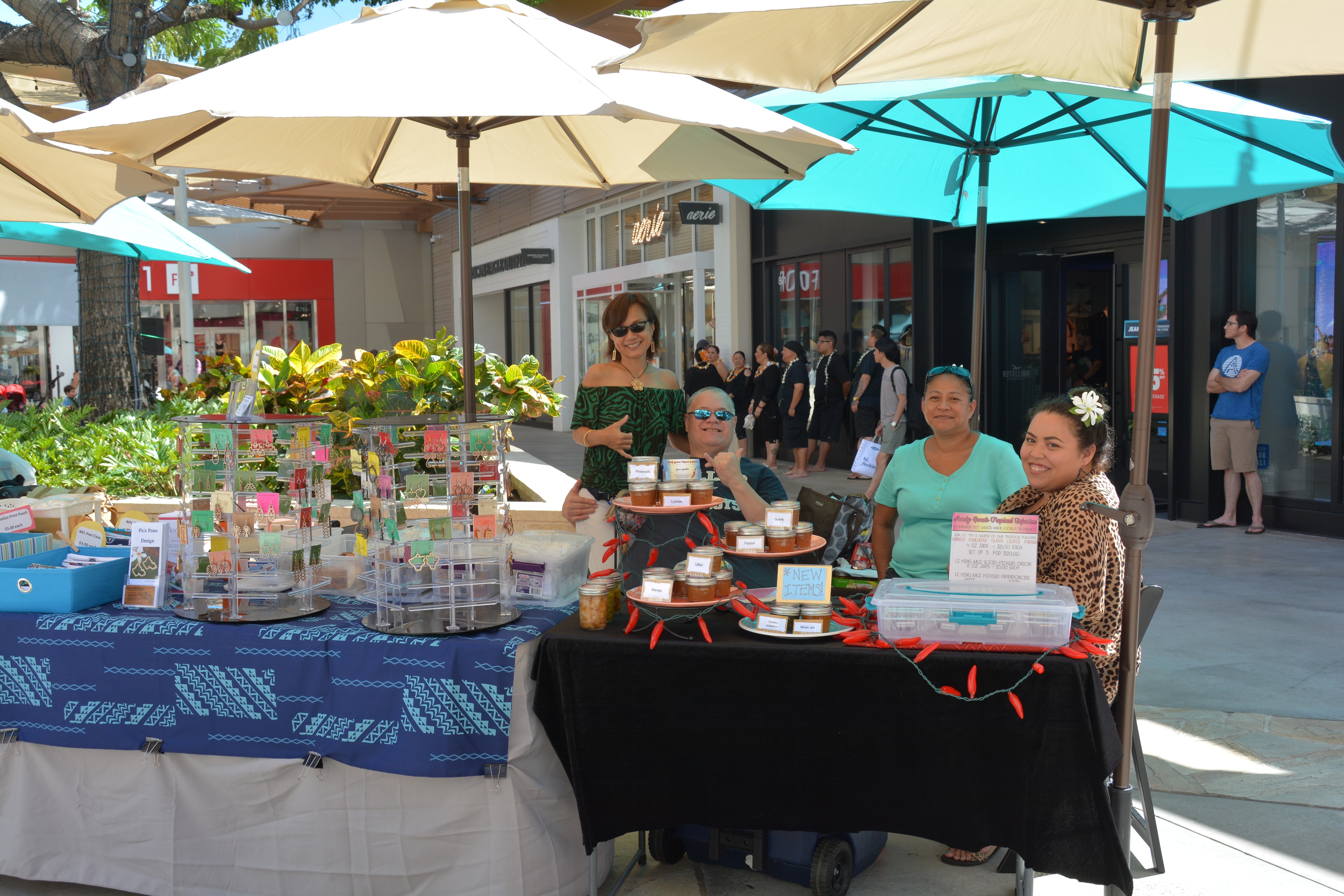 Vendors at outdoor market with jewelry and homemade food jars at Prince Kūhiō Day