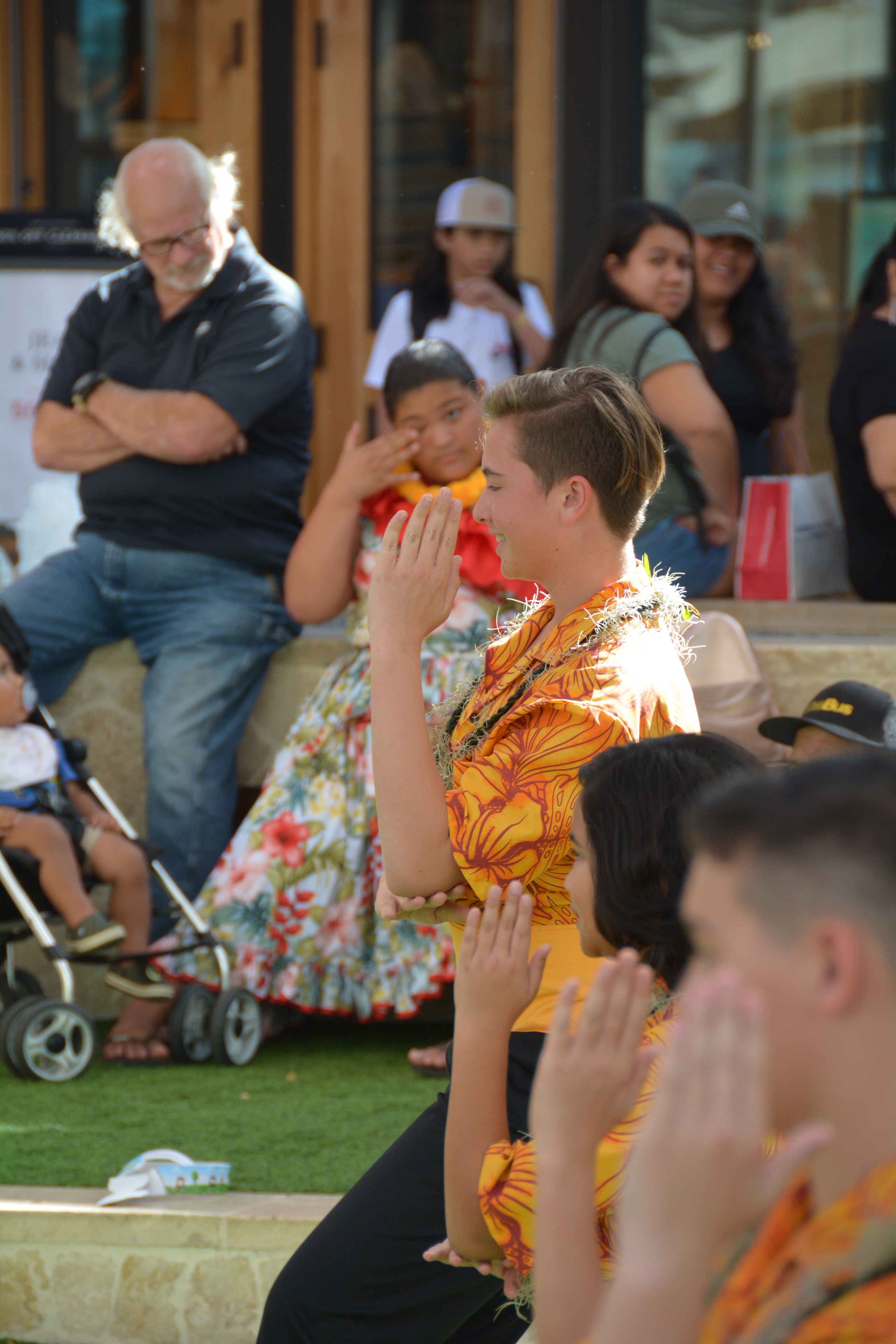 Young male dancer in orange floral shirt with hands in prayer position performing hula