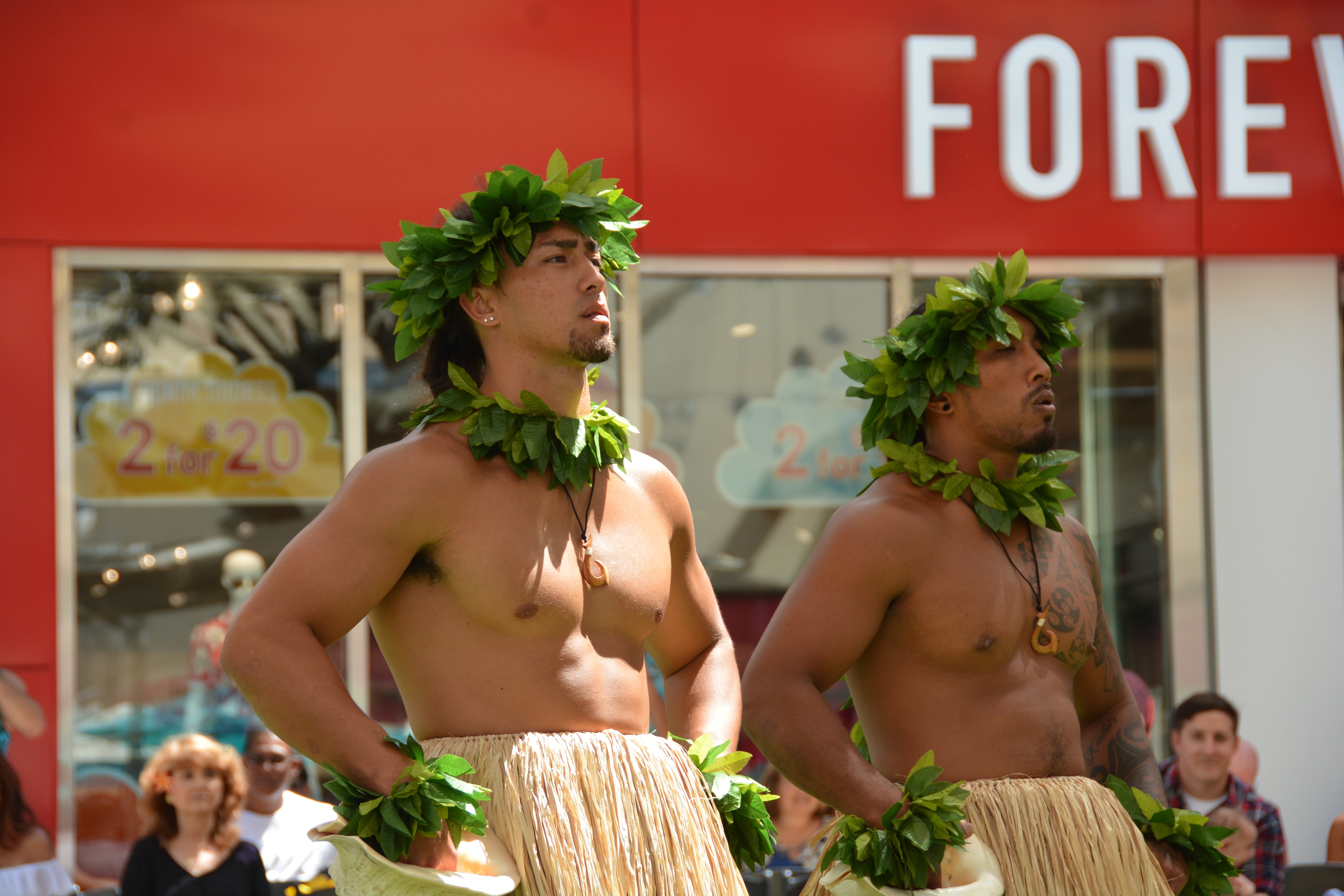 Two Hawaiian male dancers in ti leaf lei and grass skirts performing