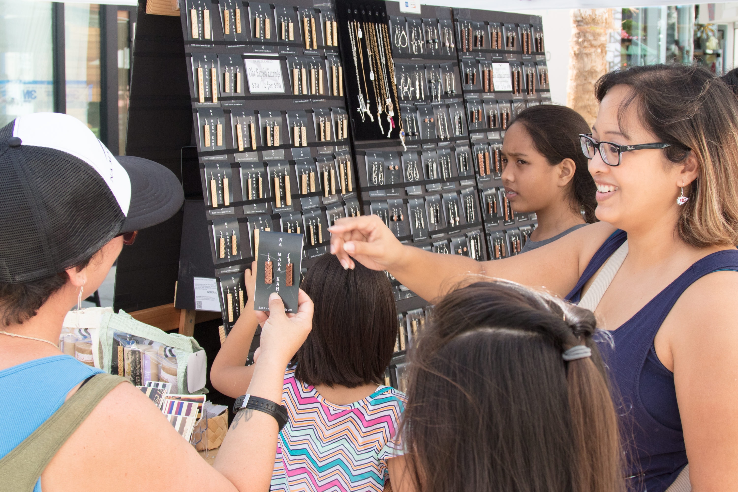 Customers browsing jewelry display at market stall